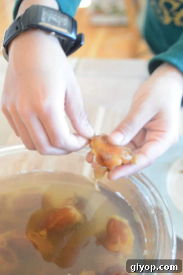 A hand gently removing skin from a soaked date, highlighting the ease of peeling after hot water treatment