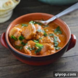 An overhead view of a bowl with chicken tikka masala on a wooden surface.