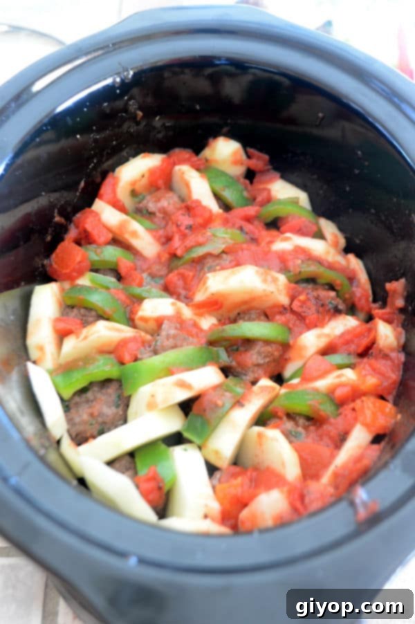 A bowl of food filled with meatballs and vegetables, covered in tomato sauce, ready for the slow cooker.