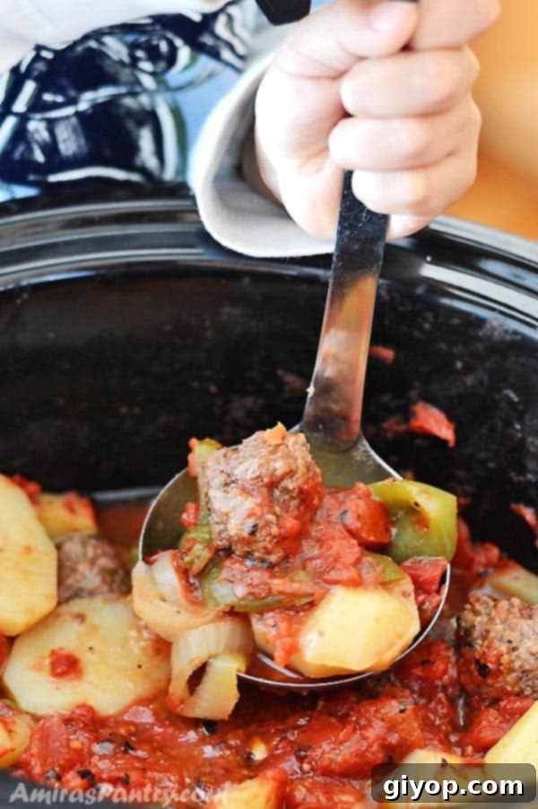 A child's hand holding a ladle and scooping some saucy meatballs and potatoes from the slow cooker, ready to eat.