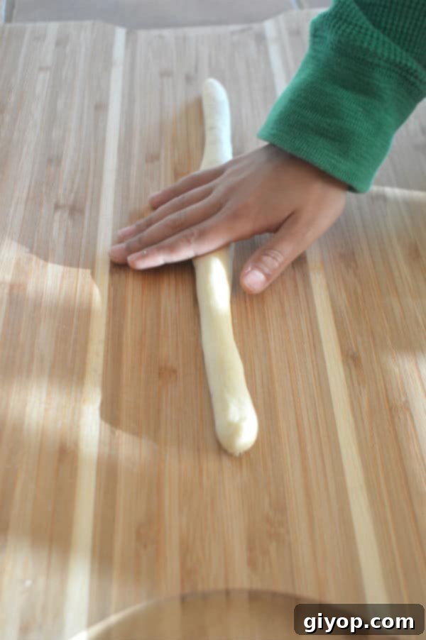 Crispy Sesame Breadsticks 6 A hand shaping a breadstick on a wooden cutting board, demonstrating the rolling technique.