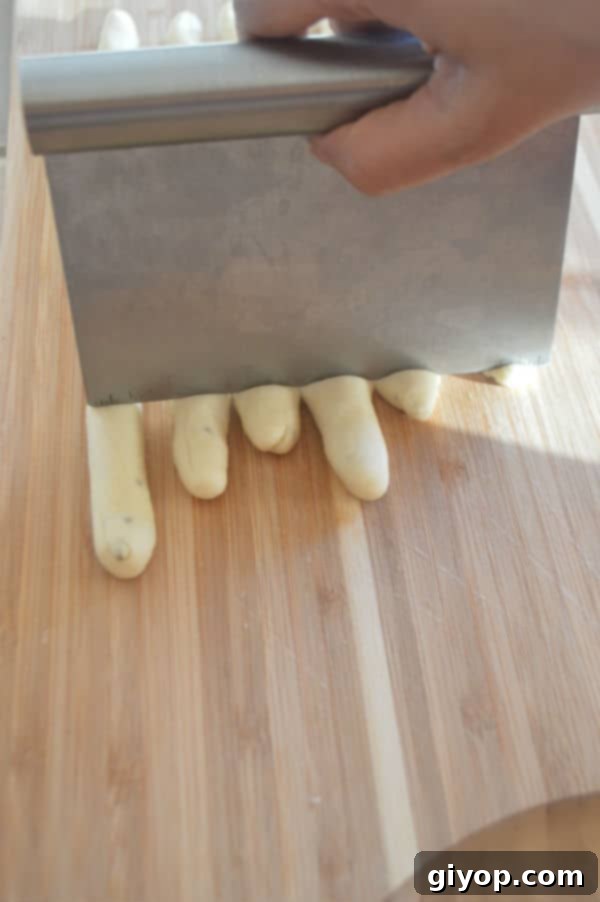 Crispy Sesame Breadsticks 7 A wooden cutting board, with shaped breadsticks being cut into pieces to ensure even length.