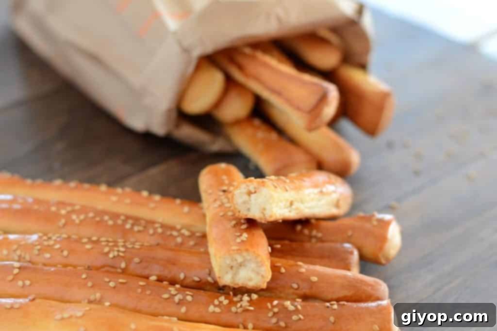 Crispy Sesame Breadsticks 9 Crispy Bo'somat breadsticks artfully arranged on a wooden table, with a brown bag filled with more breadsticks in the background, showcasing their delicious appeal.