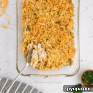 A top view of a golden-brown poppy seed chicken casserole on a white counter, with a serving spoon.