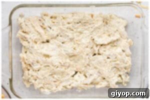 The creamy chicken poppyseed mixture spread evenly at the bottom of a glass casserole dish.