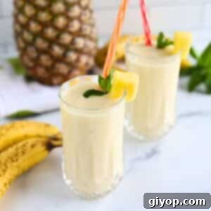 Two tall glasses of a vibrant and creamy banana pineapple smoothie, garnished attractively.