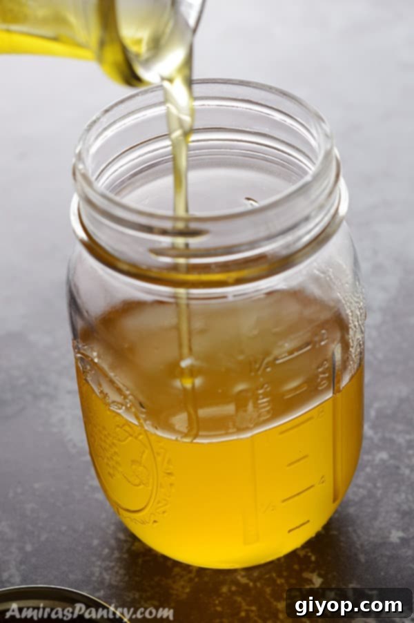 Crafting Golden Ghee from Butter 3 Pouring ghee into a mason jar with the lid on the side.