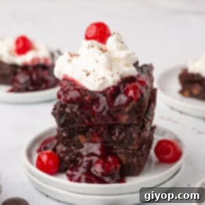 Three Black Forest Brownies stacked on top of each other on a white plate, showcasing the cherry swirl and chocolate topping.