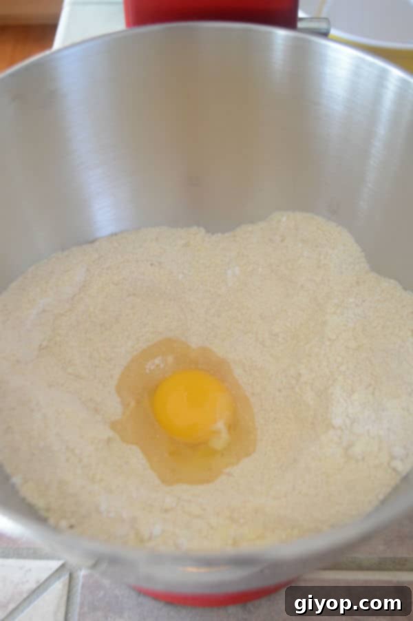 A metal mixing bowl with dry ingredients, showing a freshly cracked egg added to the mixture.