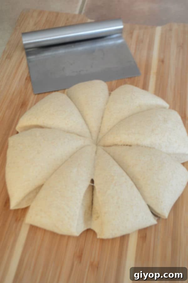 A wooden cutting board with a risen dough cut into eight equal portions, alongside a dough cutter.