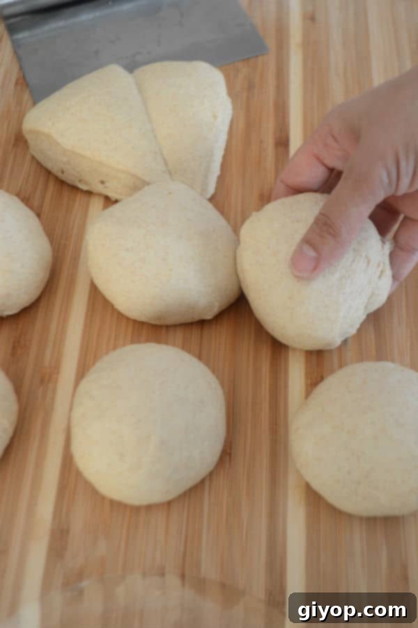 A hand gently shaping a portion of dough into a smooth, round ball on a wooden cutting board, preparing it for flattening.