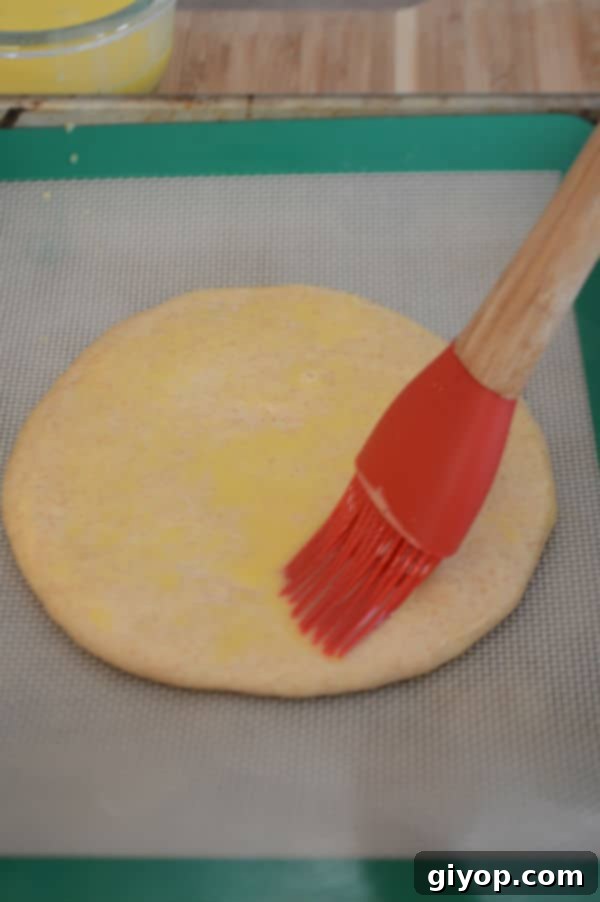 A close-up of a round dough disc resting on parchment paper, brushed evenly with an egg wash, ready for scoring.