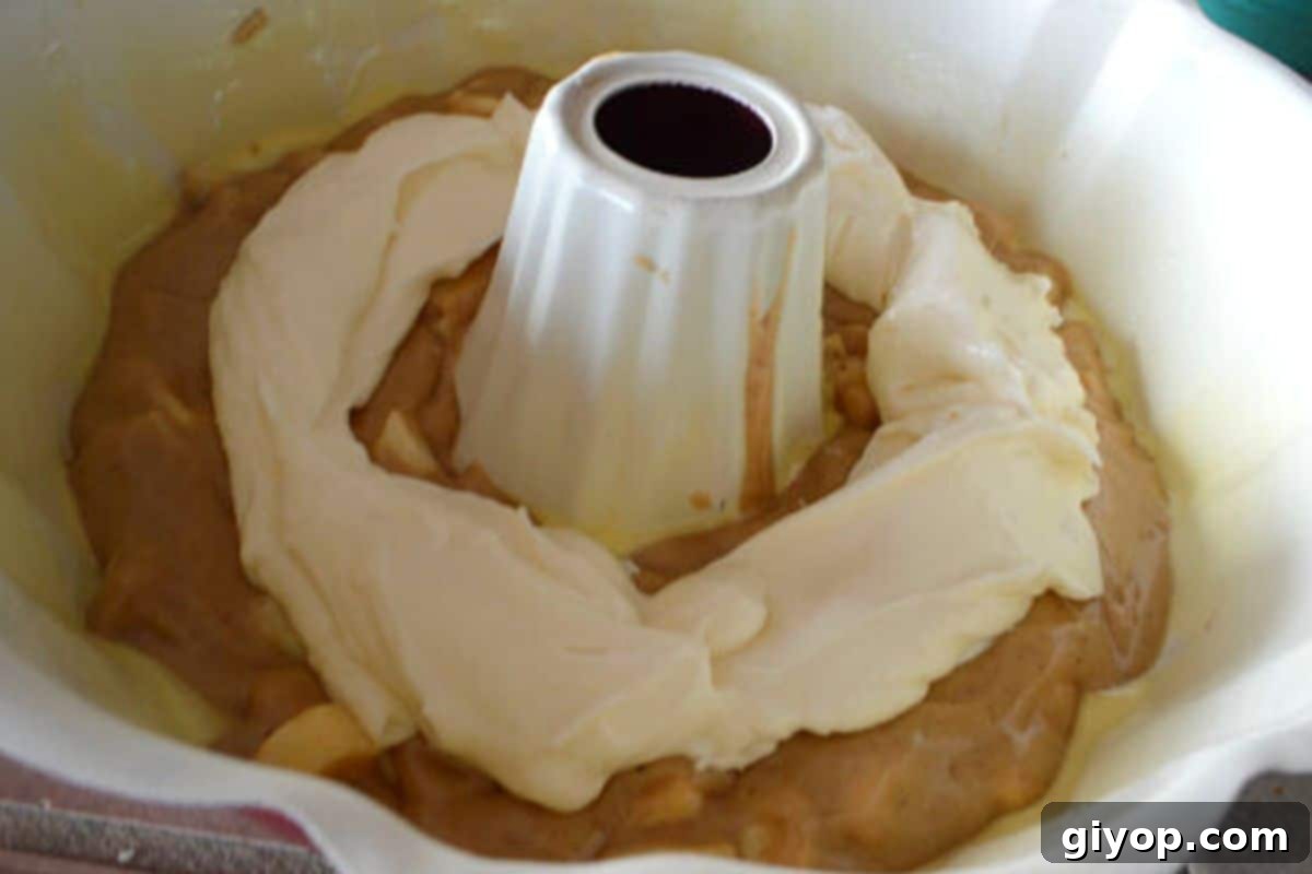 A photo showcasing the layered assembly of the Bundt cake, with cake batter topped with the cream cheese filling before the final layer of batter.
