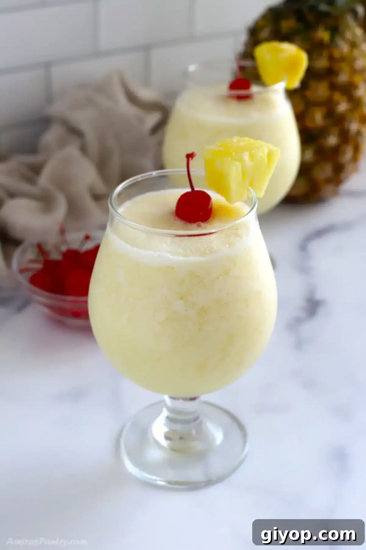 A glass of virgin pina colada with a cherry on top, sitting on a wooden surface with tropical leaves in the background.