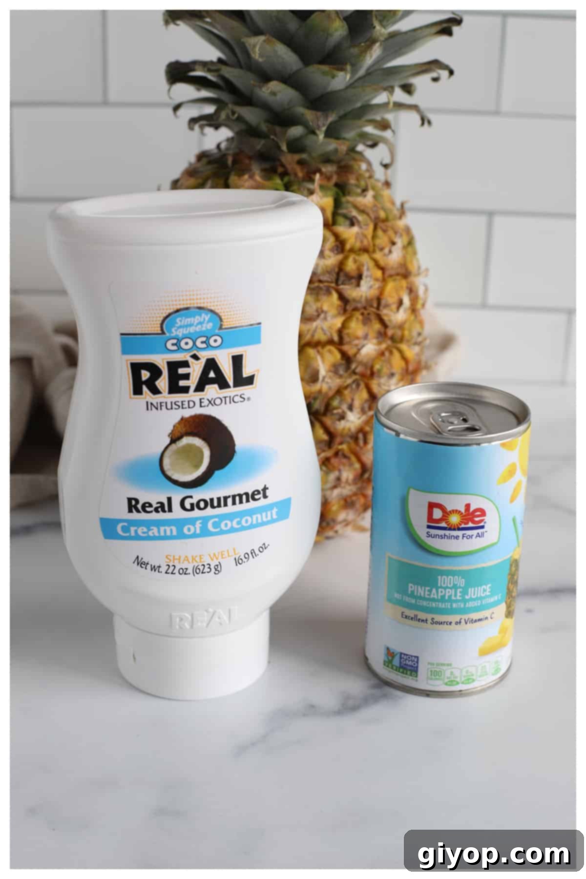 Ingredients for the Virgin Pina Colada arranged on a kitchen counter: pineapple juice, cream of coconut, ice, and maraschino cherries.