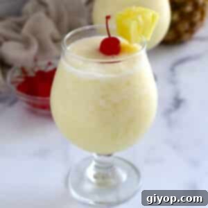 A close up image of a glass of pina colada, garnished with a cherry and pineapple wedge.
