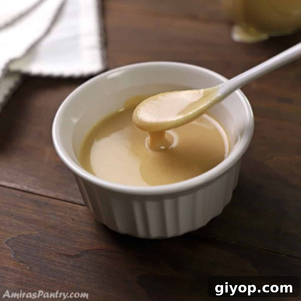 A spoon scooping some homemade tahini out of a white bowl.