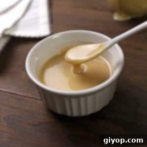 A white spoon scooping some homemade tahini out of a white bowl.