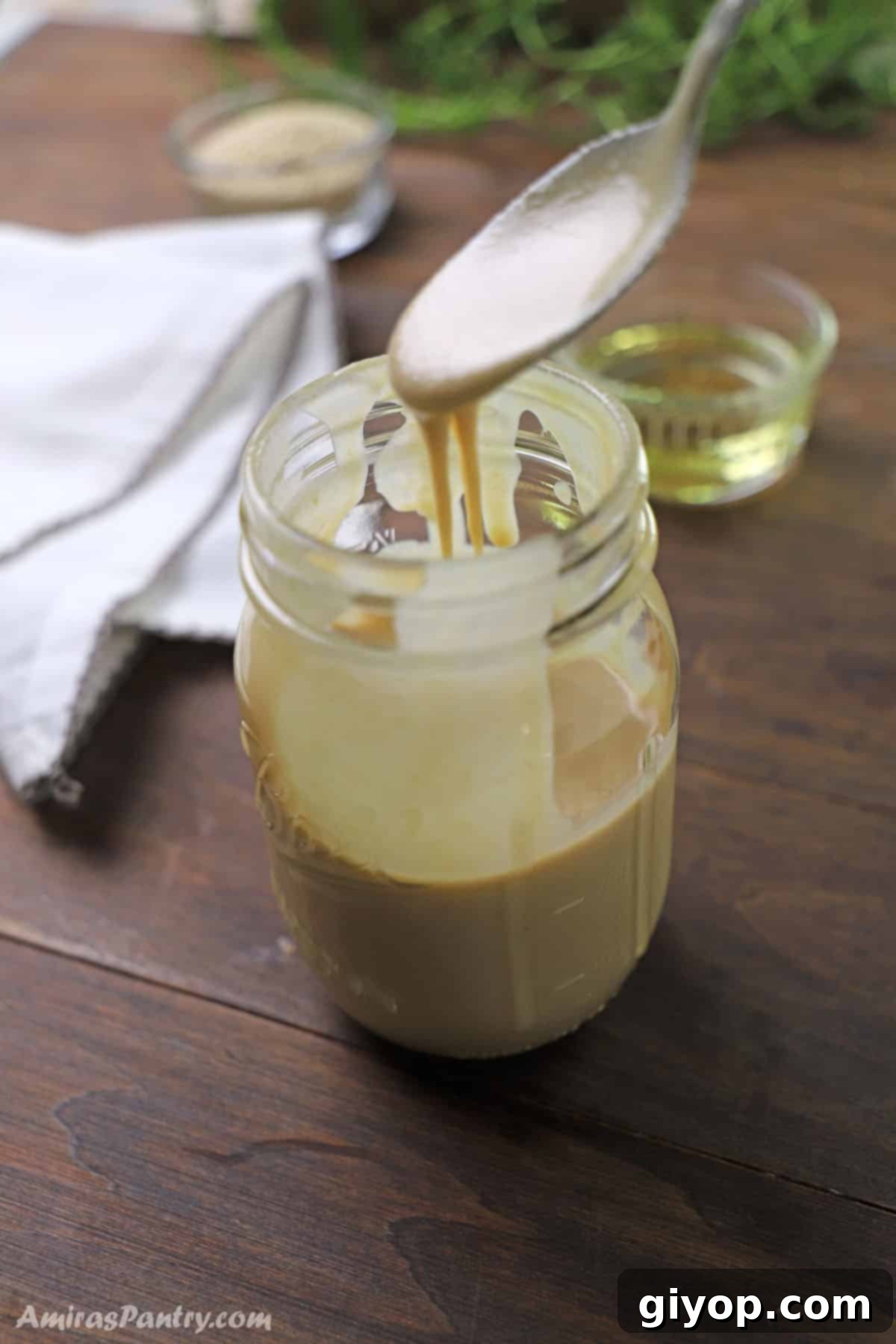 A spoon pouring some homemade tahini in a jar.
