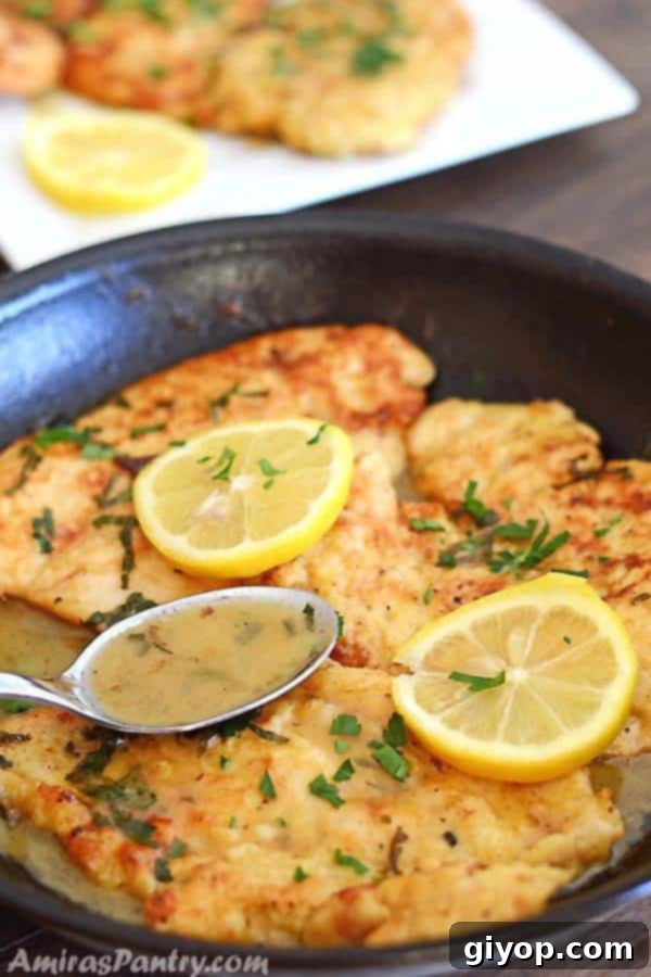 Flavorful Chicken Francese No Wine Required 2 Golden brown chicken francese cutlets in a pan, glistening with a rich, lemony butter sauce, garnished with fresh lemon rinds and parsley.
