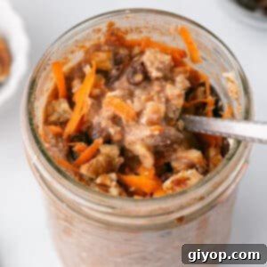 A spoon scooping some creamy carrot cake overnight oats from a glass jar, topped with nuts and coconut.