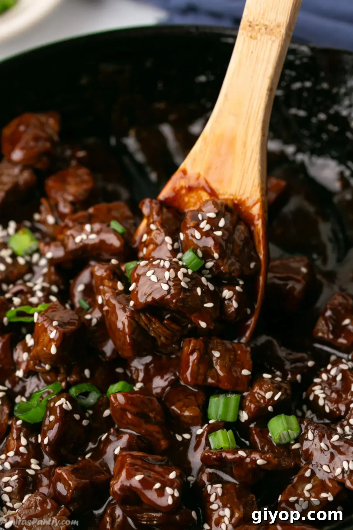 Glazed Honey Garlic Steak Bites 2 A wooden spoon scooping some glistening honey garlic steak bites from a hot skillet, ready to serve.