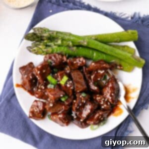 Glazed Honey Garlic Steak Bites 3 STeak bites on a white plate with steamed asparagus, showcasing the final dish.