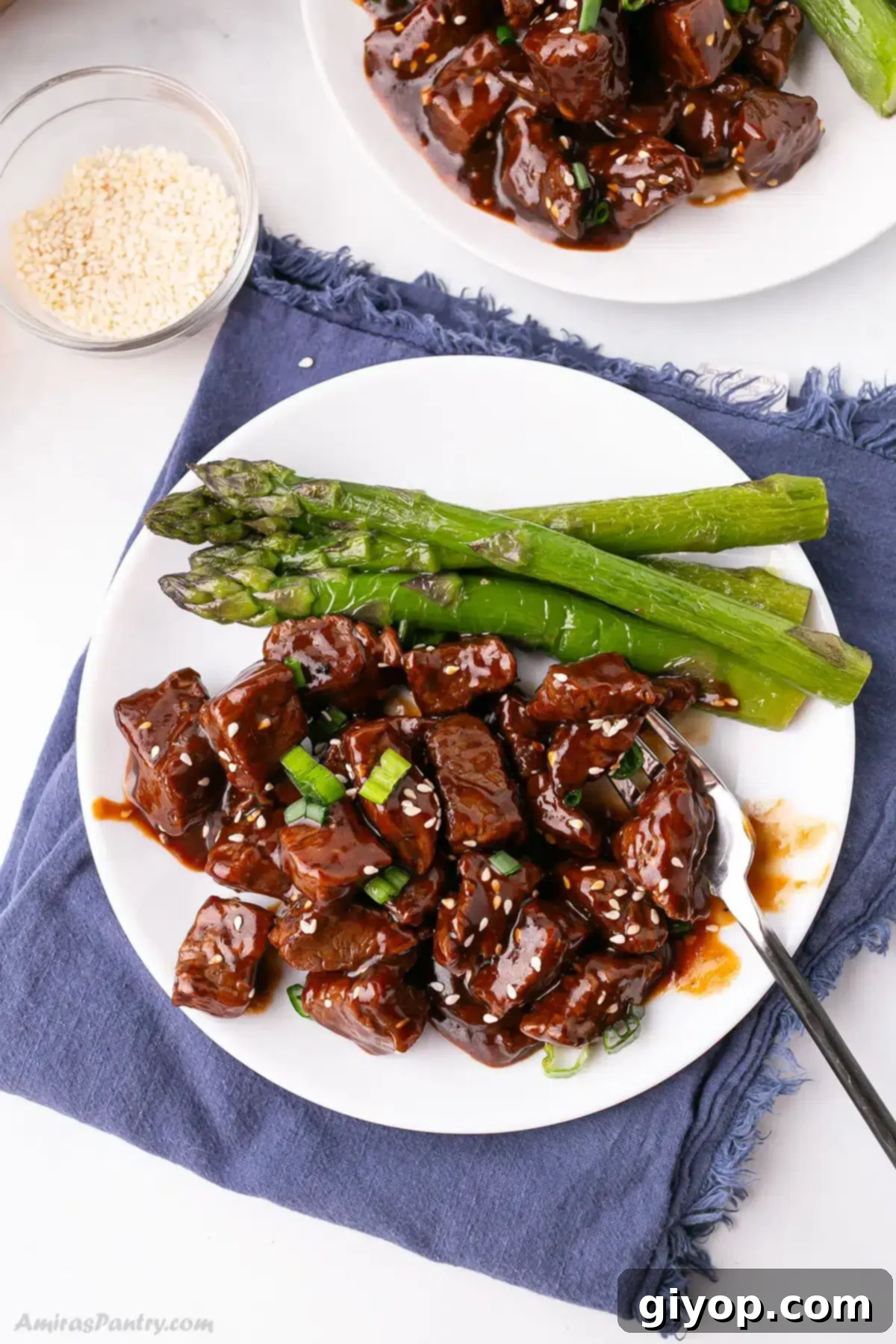 Glazed Honey Garlic Steak Bites 5 A white plate featuring perfectly cooked honey garlic steak bites garnished with fresh sesame seeds, ready to be enjoyed as a delicious weeknight dinner.