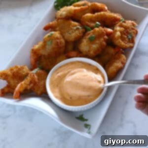 A small metal spoon with some Bang Bang sauce in a shrimp platter, ready for dipping.