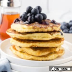 Lemon ricotta pancakes on a white plate with syrup in the back.