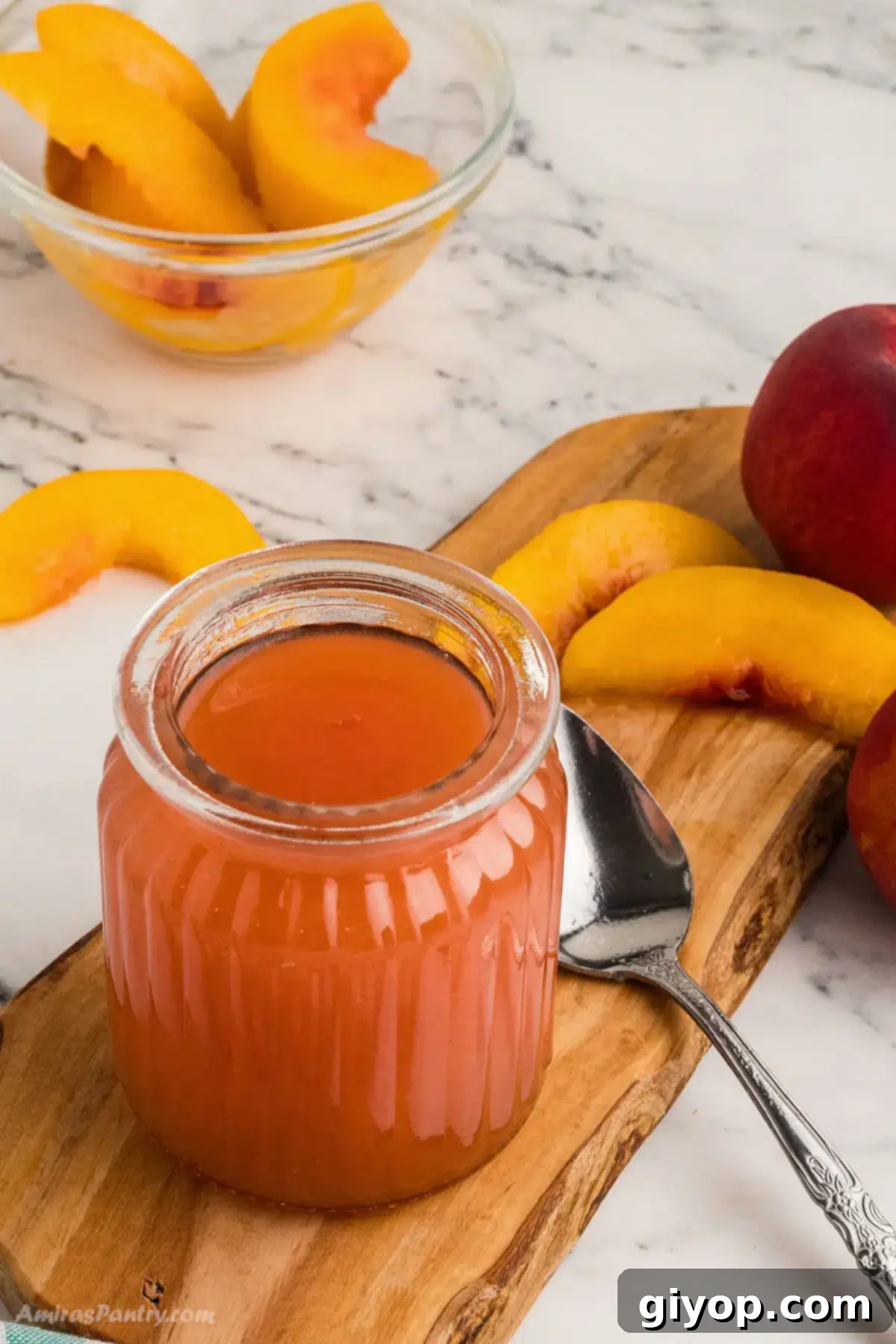 A glass jar filled with golden peach syrup, adorned with fresh peach slices and a sprig of mint, sitting on a rustic wooden board with whole peaches beside it, ready for use.