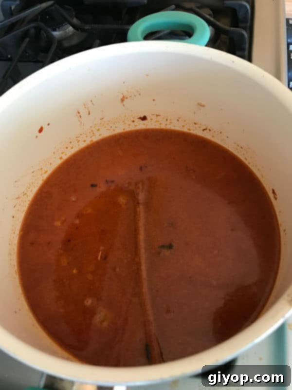 A pot of the wild rice covered with water and tomato sauce with a cinnamon stick floating on top.