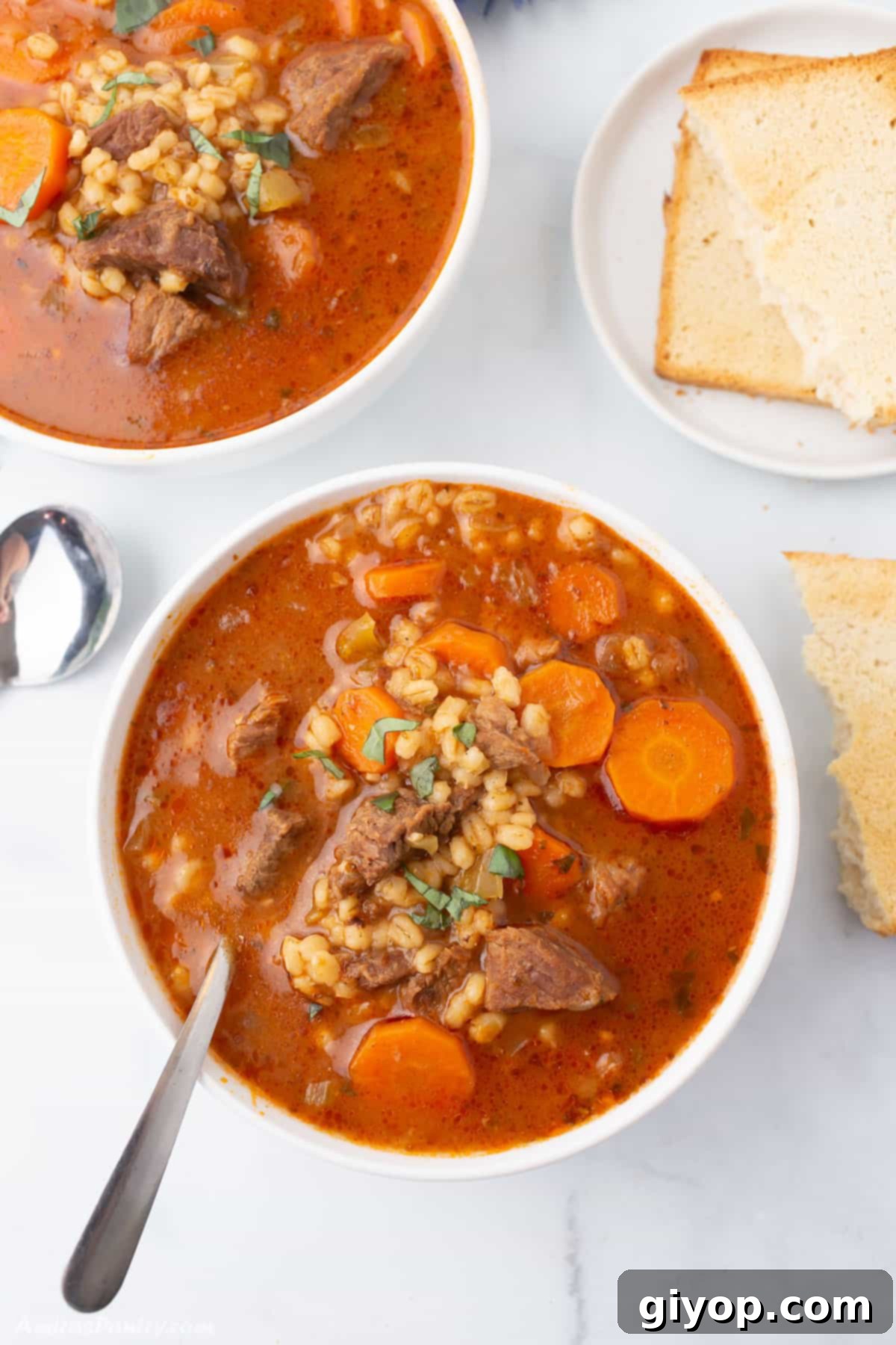 Effortless Instant Pot Soups 4 Two white bowls of beef and barley soup on a white marble table.