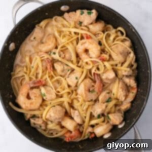 An overhead image of a large skillet with alfredo pasta with shrimp and chicken, ready to serve.