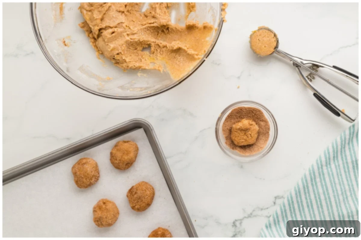A cookie sheet with cookie dough balls and a cookie scoop on the side.