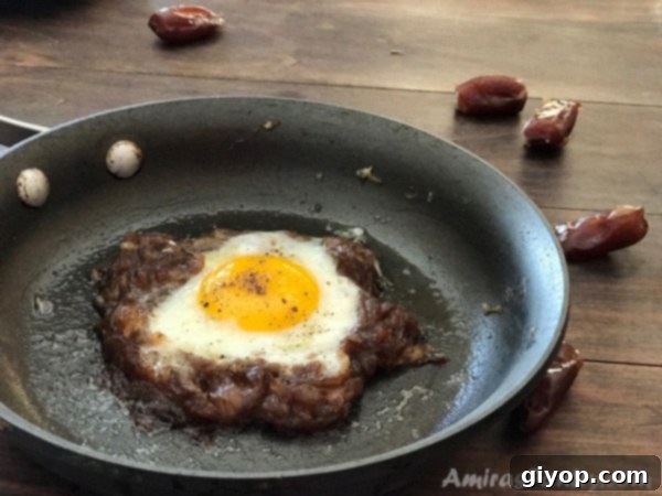 A close-up view of Egg Agwa sizzling in a non-stick pan, with the softened date paste forming a ring around the cooking egg, perfectly illustrating the simple and quick preparation process.