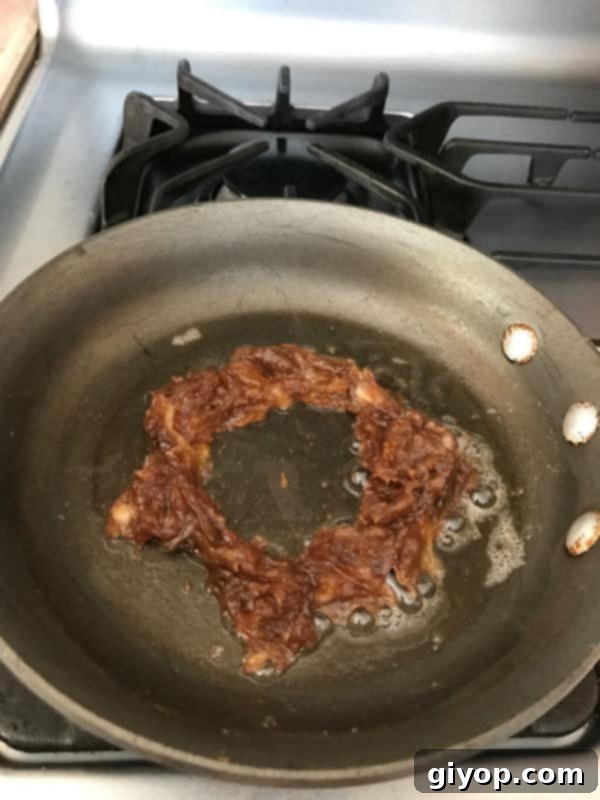 The softened date paste (Agwa) expertly shaped into a perfect, uniform ring within the skillet, creating a neat well in the center specifically designed for the egg.