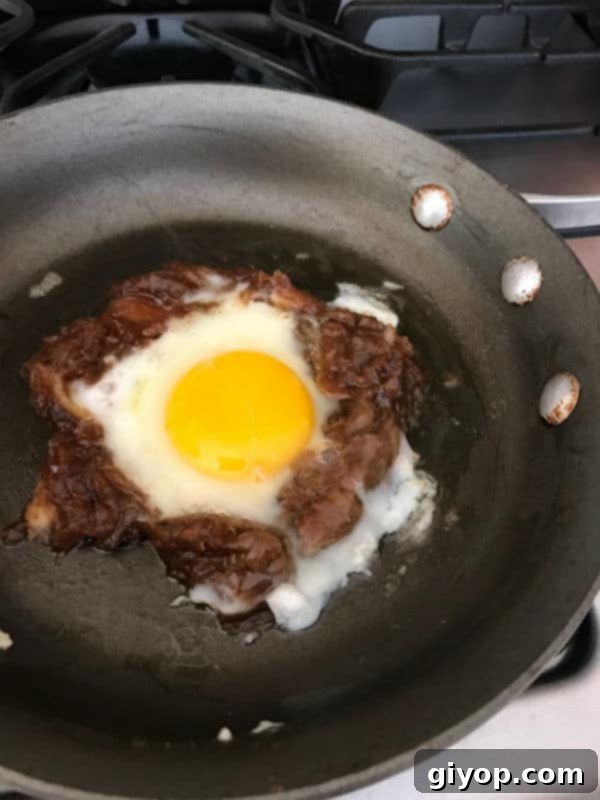 A fresh, large egg carefully cracked into the butter-filled center of the Agwa ring, now ready to gently cook on minimum heat until perfectly set.