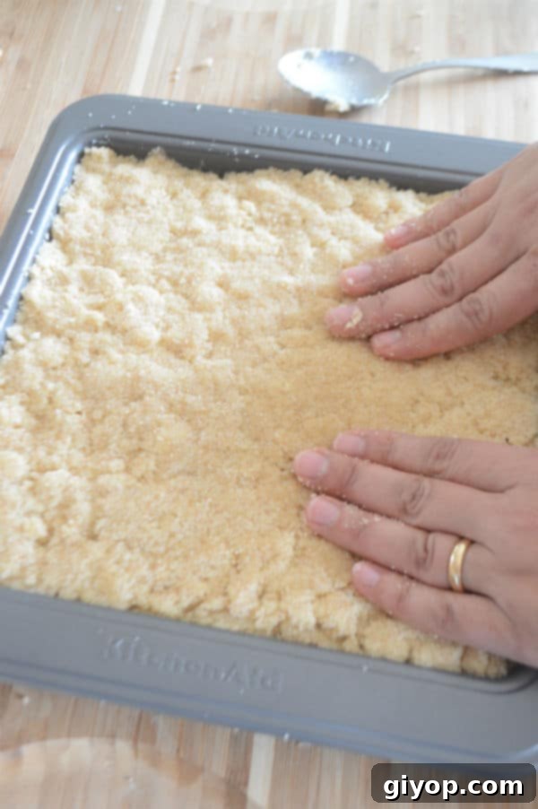 Pistachio-Packed Maamoul with Velvety Ashta 12 A hand gently pressing the remaining semolina mixture over the Ashta layer, sealing the filling, preparing the dish for baking.