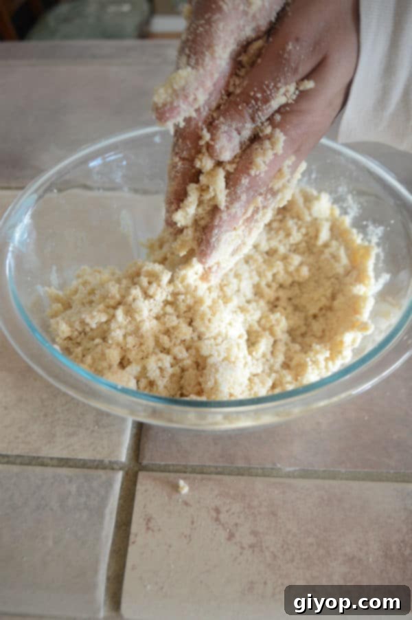 Pistachio-Packed Maamoul with Velvety Ashta 6 A hand gently mixing the semolina and butter mixture in a bowl, ensuring all granules are coated, creating a sandy texture.