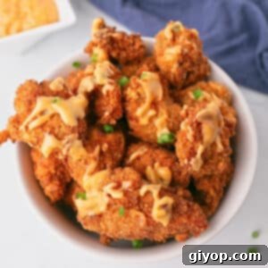 An overhead image of a bowl with fried chicken bites drizzled in bang bang sauce.