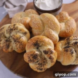 A pile of kaiser rolls on a wooden board with cheese.