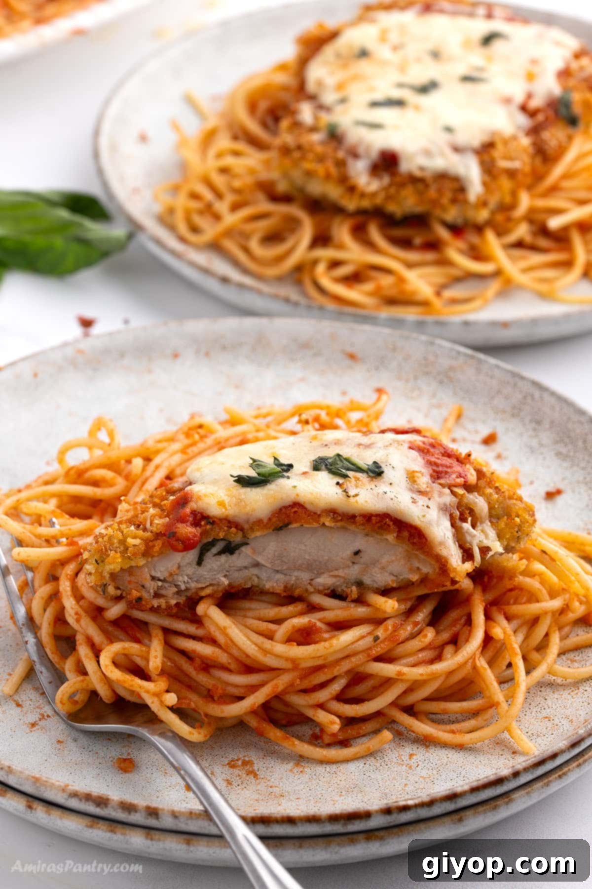 Two dinner plates showcasing spaghetti topped with vibrant tomato sauce and a generous serving of cheesy Chicken Parmesan Thighs, garnished with fresh basil.