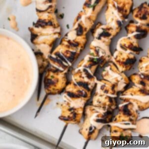 Sheet pan with grilled chicken skewers drizzled with bang bang sauce.