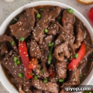 Tender Slow Cooker Mongolian Beef 2 An overhead image of a white plate with succulent Slow Cooker Mongolian Beef garnished with sesame seeds and fresh green onions.