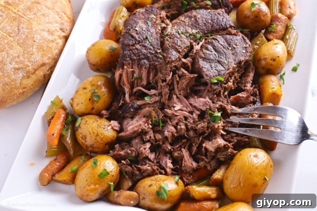 A close-up image of the slow cooker pot roast with gravy and vegetables in a serving dish.