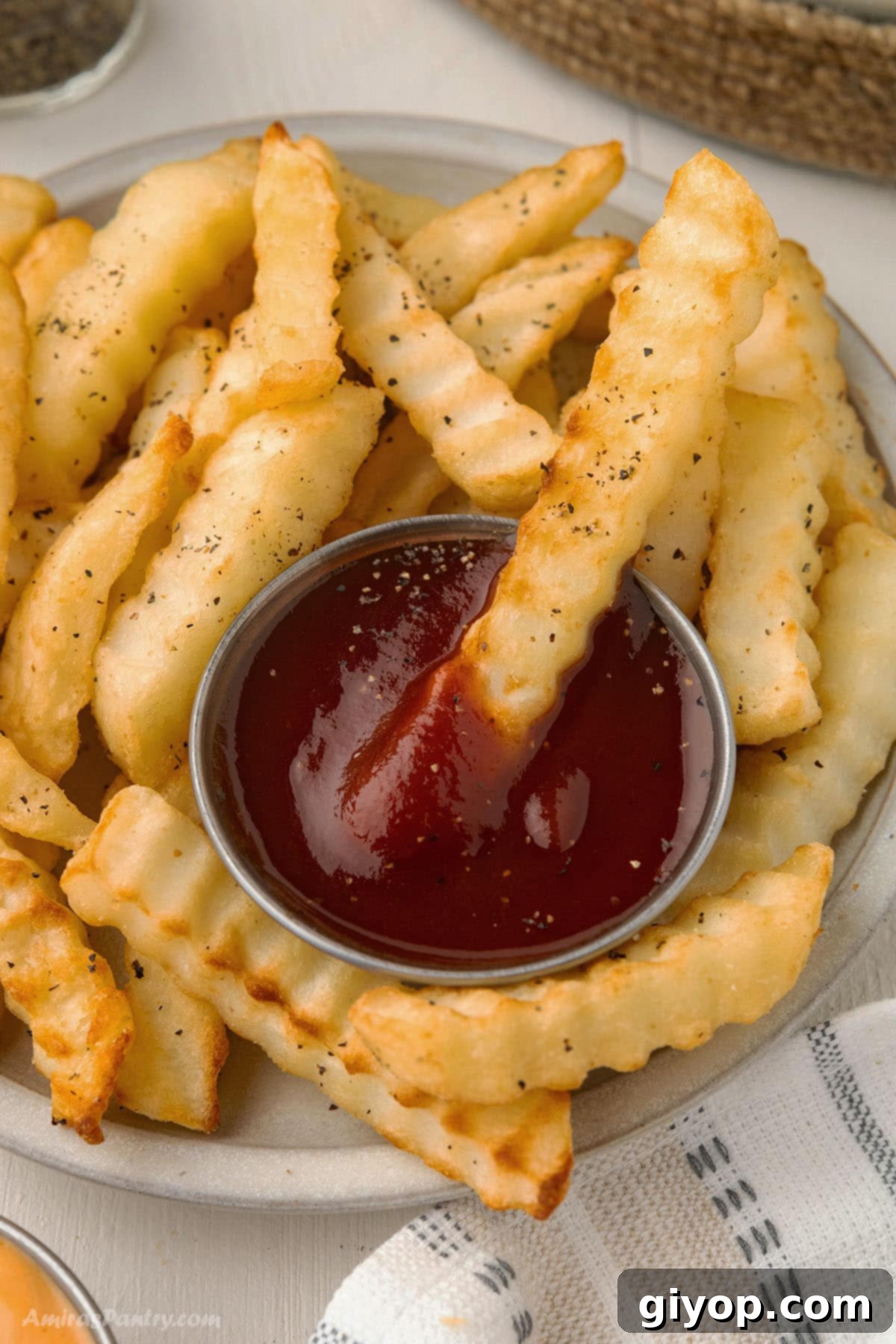 An overhead image of a plate of french fries with ketchup bowl in the middle.