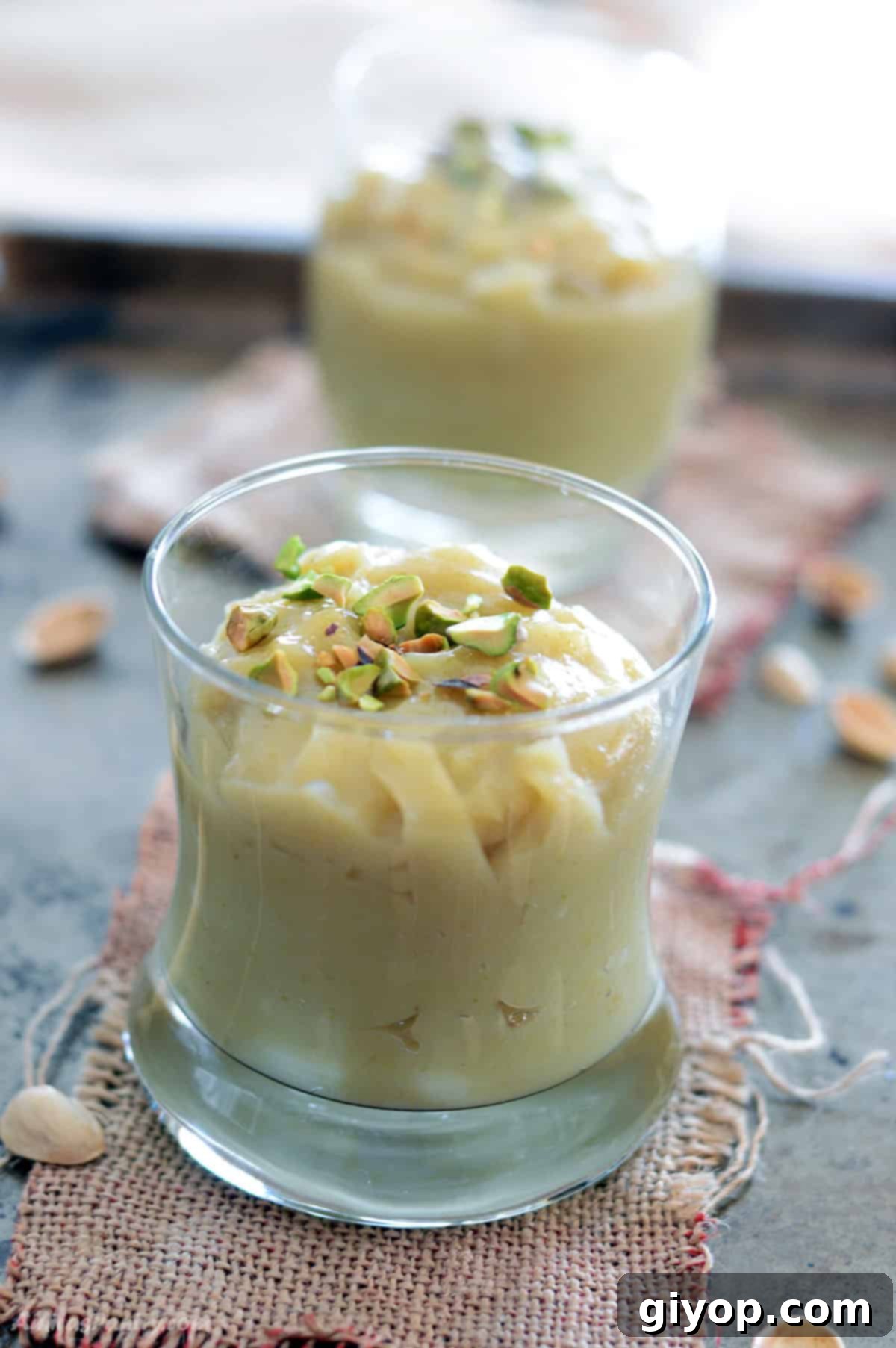 Velvet Pistachio Delight 2 A close-up view of a glass cup filled with luscious homemade pistachio pudding, beautifully garnished with finely chopped pistachios. The natural, subtle green hue and creamy texture of the pudding are prominently displayed, inviting a delightful taste.