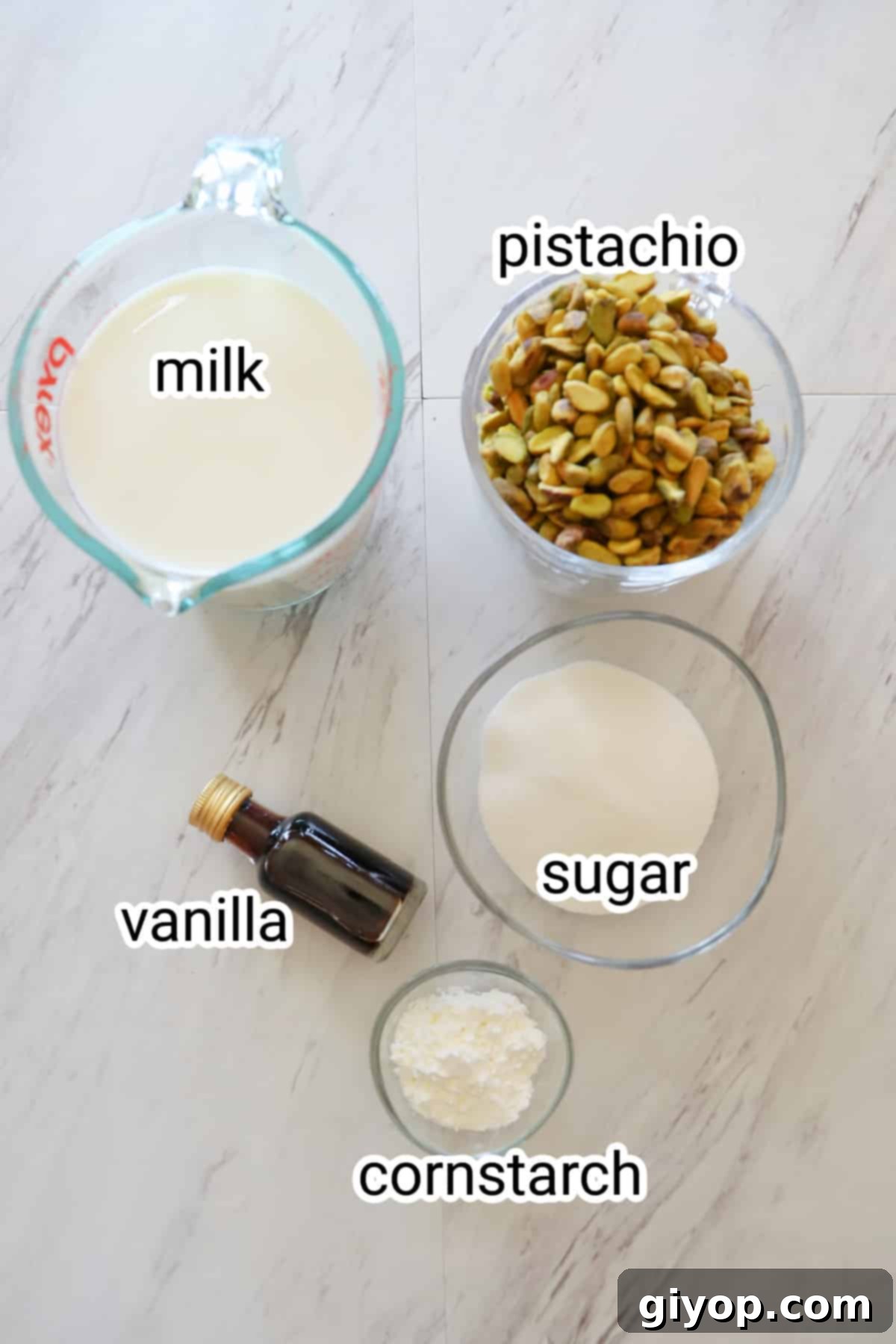 Velvet Pistachio Delight 3 A perfectly arranged flat lay of five key ingredients for homemade pistachio pudding on a pristine white kitchen counter: a bowl of unsalted raw pistachios, a bottle of whole milk, a measuring cup of granulated sugar, a small bottle of vanilla extract, and a container of cornstarch.