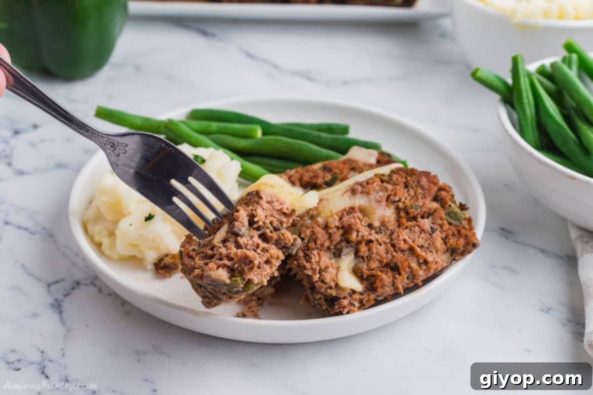 A close-up of a generous slice of Philly Cheesesteak Meatloaf, showcasing the melted cheese and juicy interior, served on a plate as a comforting meal.